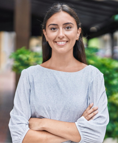 "Professional woman in light gray blouse smiling confidently with arms crossed in business setting"