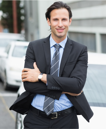 "Professional businessman in dark suit smiling confidently with arms crossed in urban setting"