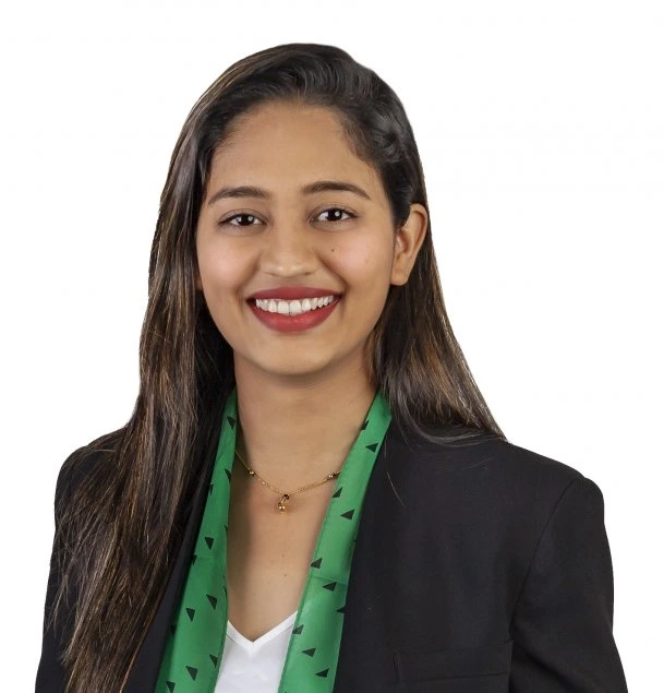 "Professional headshot of a young woman in business attire with black blazer and green patterned scarf smiling warmly at camera"