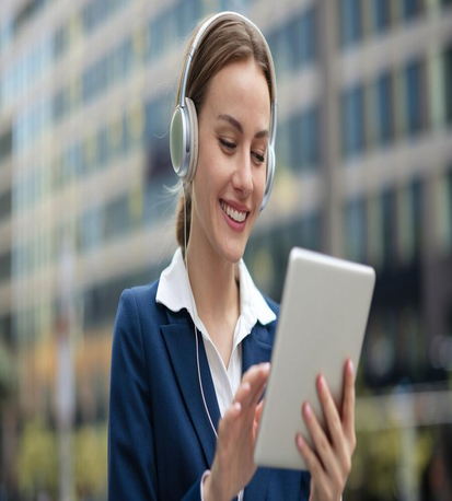 "Professional businesswoman using tablet while wearing headphones outdoors near office building"