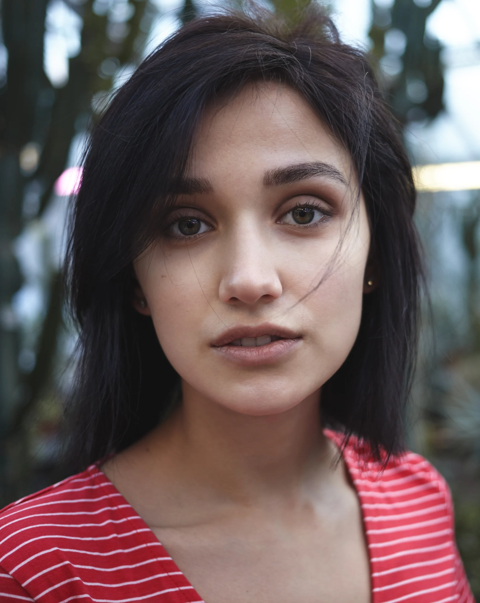 "Young woman in red striped top with natural makeup outdoors against blurred forest background"